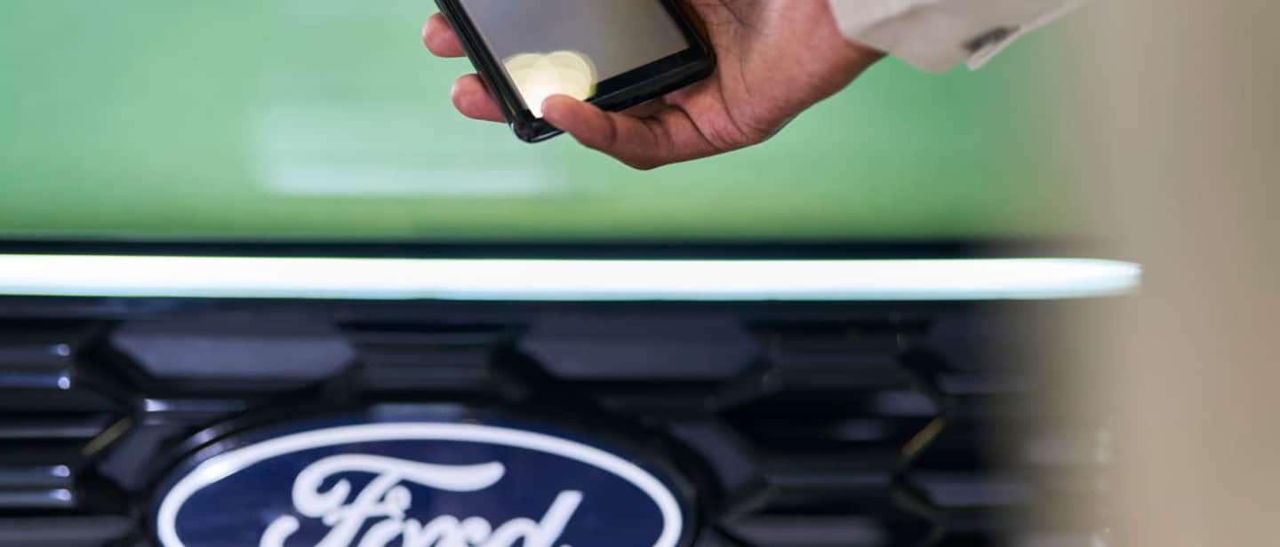 Persona sosteniendo un teléfono con la aplicación Ford abierta, delante de un Ford