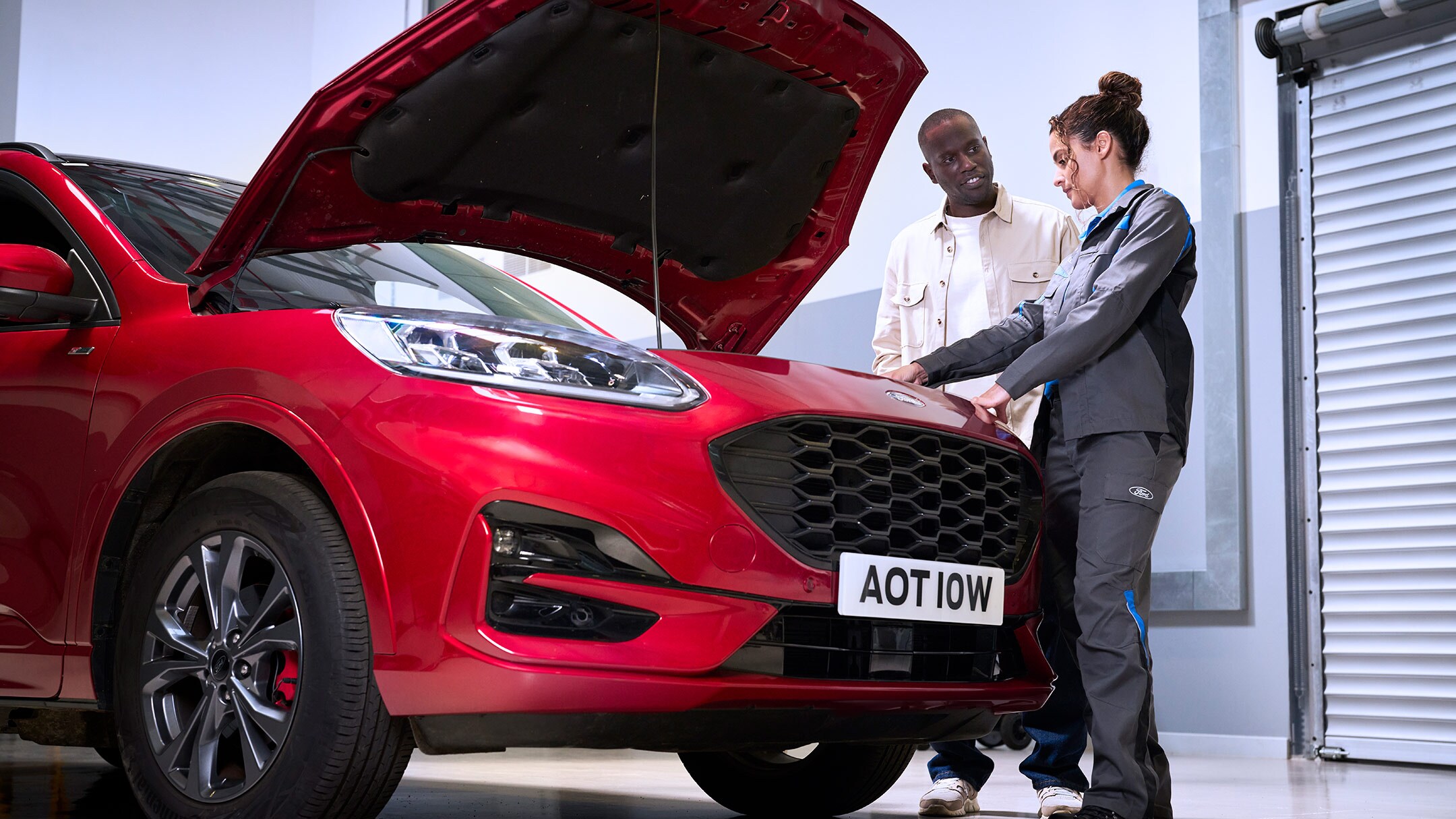 Ford Kuga rojo con capó abierto, un técnico y una persona inspeccionando el compartimento del motor