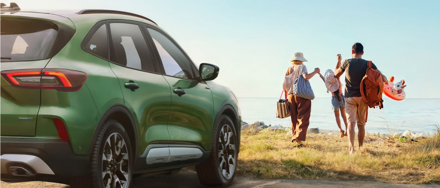 Ford Kuga verde estacionado, con una familia caminando hacia la playa llevando artículos de playa.