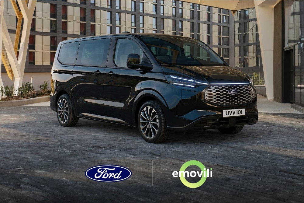 Un Ford Tourneo Custom negro aparcado en la entrada de un edificio moderno visto desde la parte delantera.