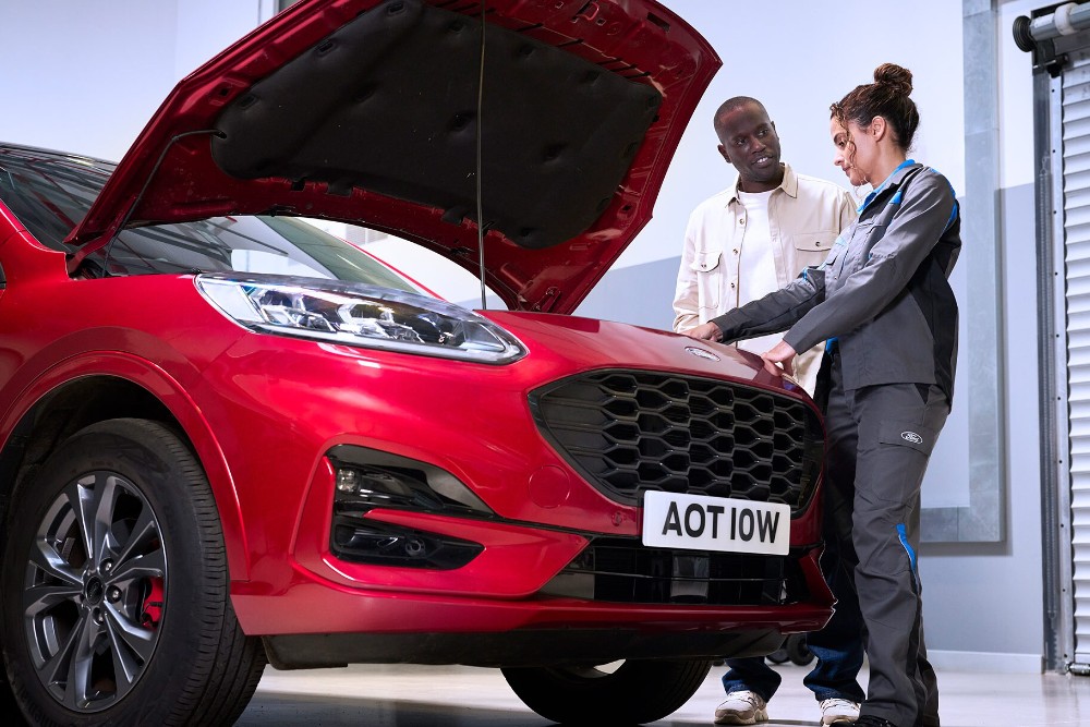 Ford Kuga rojo con capó abierto, un técnico y una persona inspeccionando el compartimento del motor