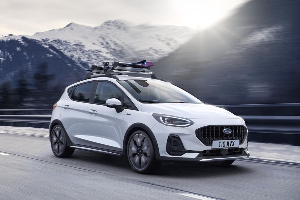 Un Ford Fiesta blanco con portaequipajes de techo circula por una carretera de montaña.
