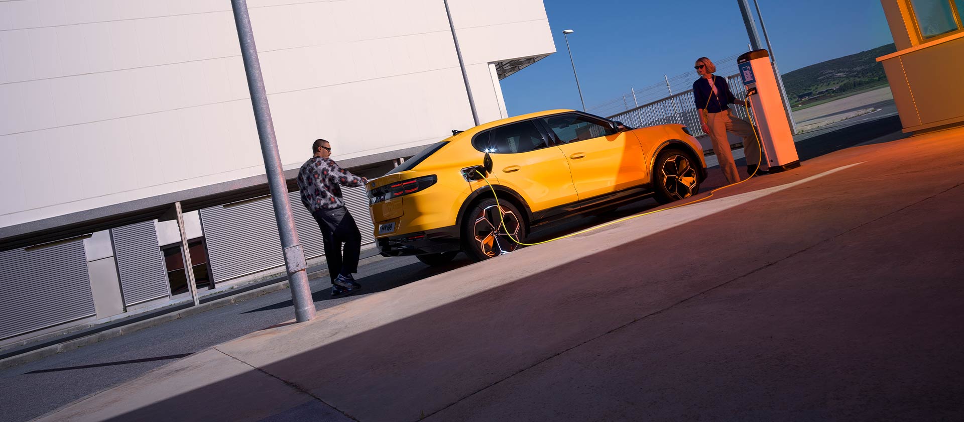 Personas cargando un Ford Capri EV amarillo en una estación de carga pública.
