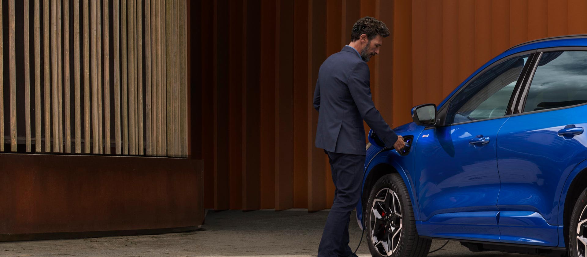 Una persona conectando un coche híbrido enchufable de Ford a un cable de carga doméstico de un vehículo eléctrico.