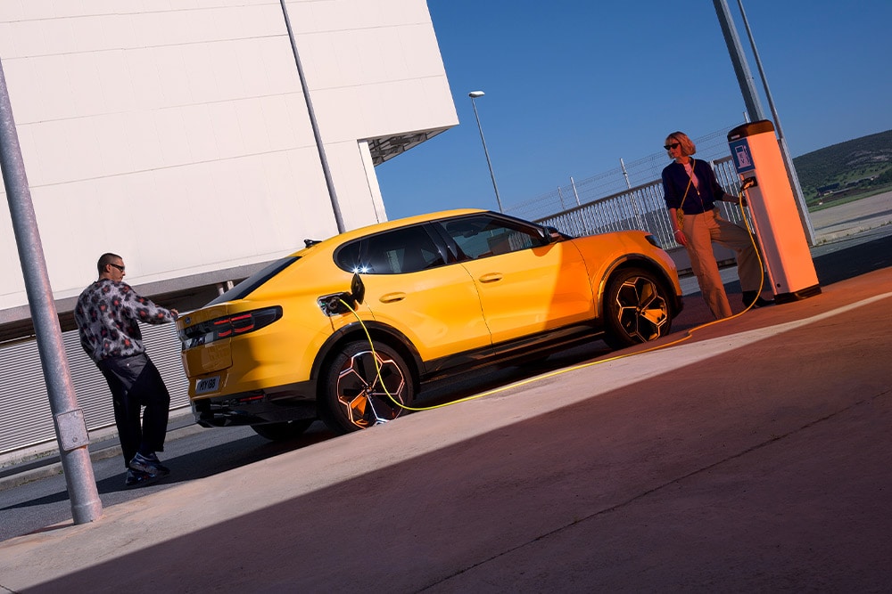 Personas cargando un Ford Capri EV amarillo en una estación de carga pública.