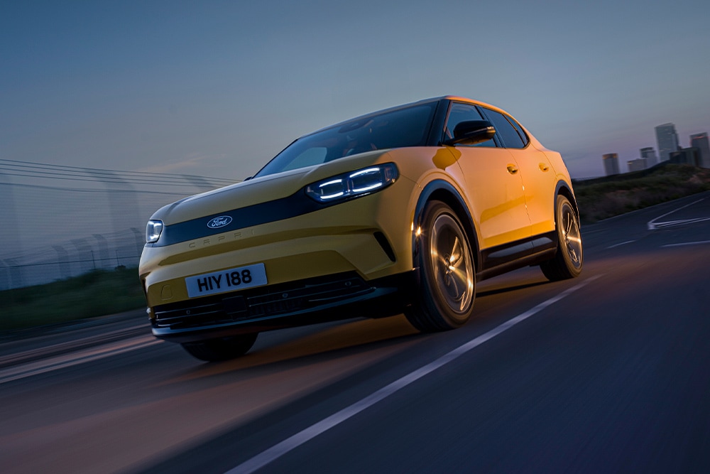 Un coche eléctrico Ford Capri amarillo circulando por una carretera abierta.