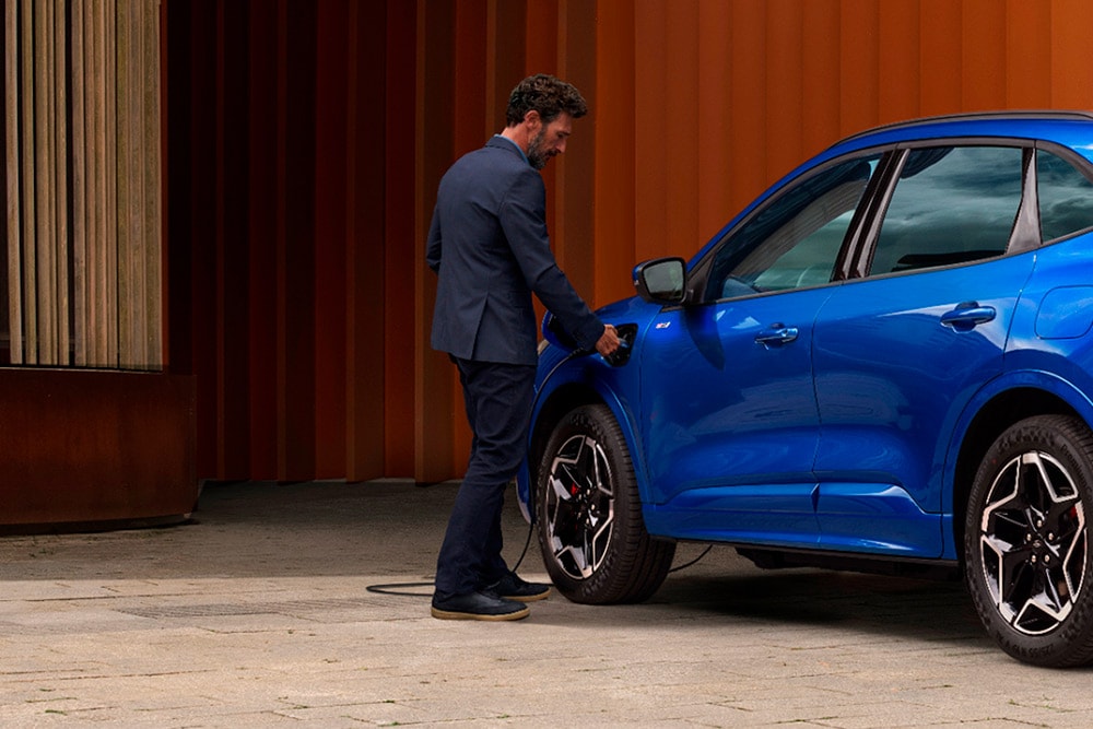 Una persona conectando un cable de carga doméstica de un vehículo eléctrico a un automóvil híbrido enchufable de Ford.