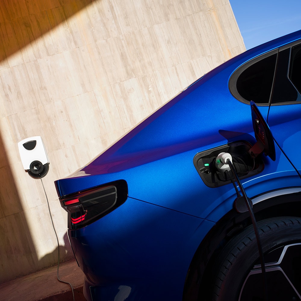 Vista trasera de un vehículo eléctrico Ford Capri azul conectado a un punto de carga doméstico de vehículos eléctricos.