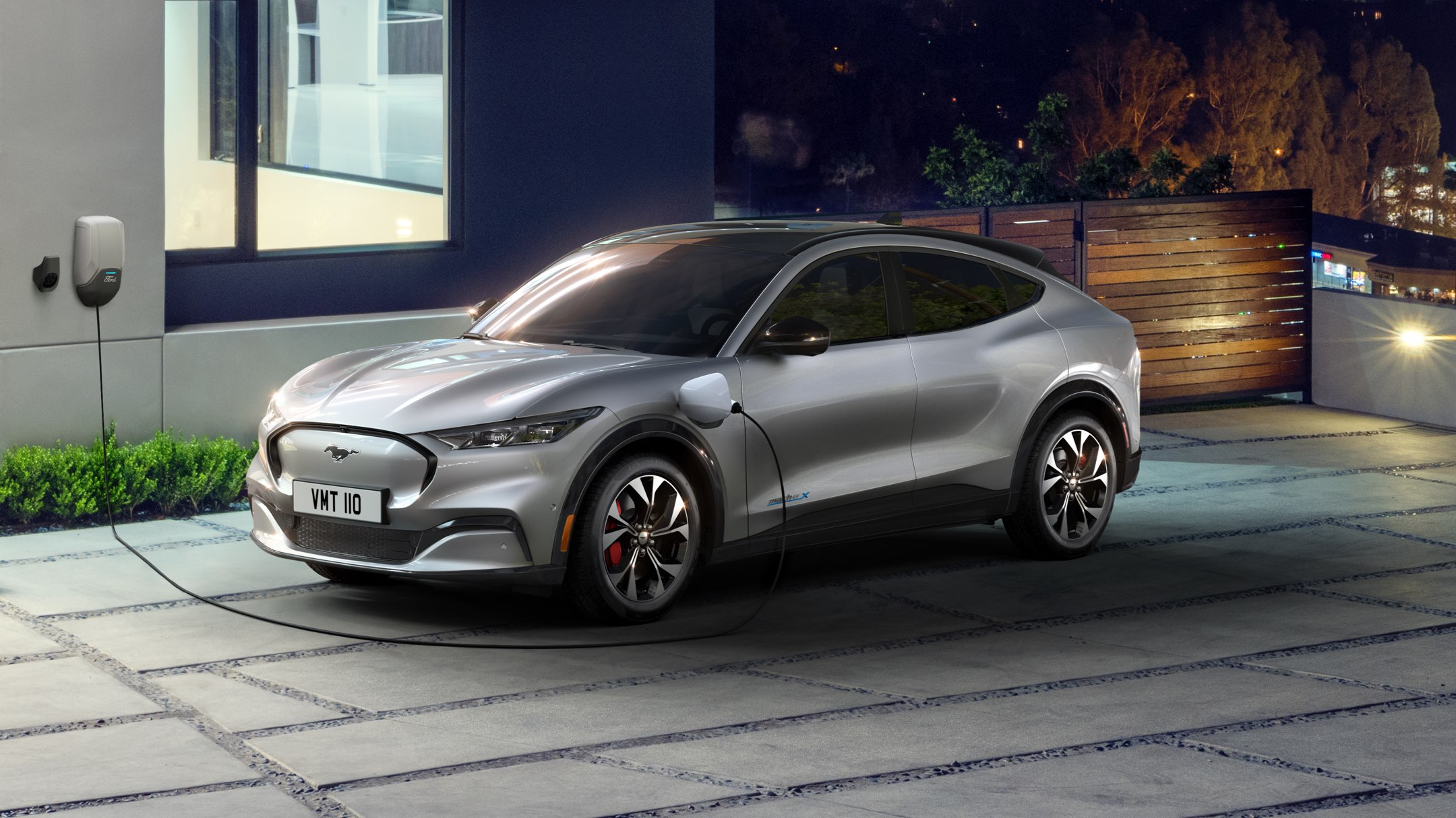 Grey Mustang Mach-E charging next to a house