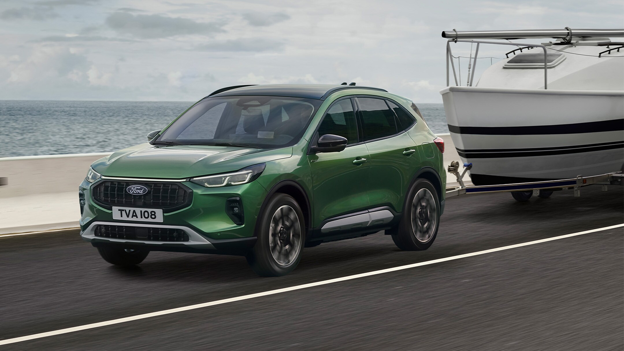 Ford Kuga verde remolcando un pequeño barco por una carretera de la costa.