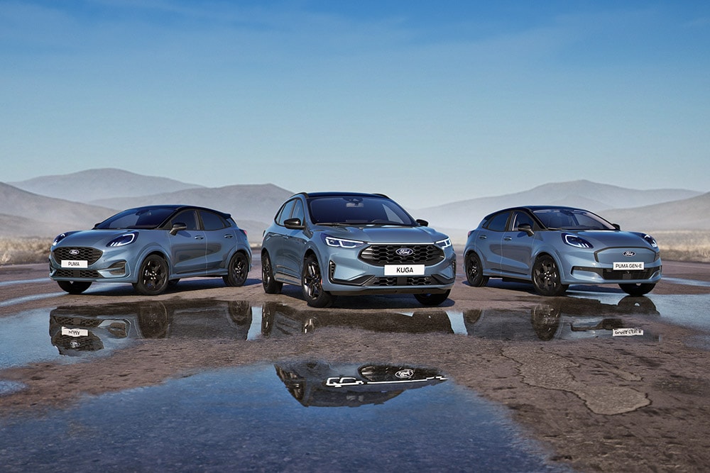 Un Ford Puma, un Ford Kuga y un Ford Puma Gen-E aparcados en una carretera mojada con montañas de fondo.