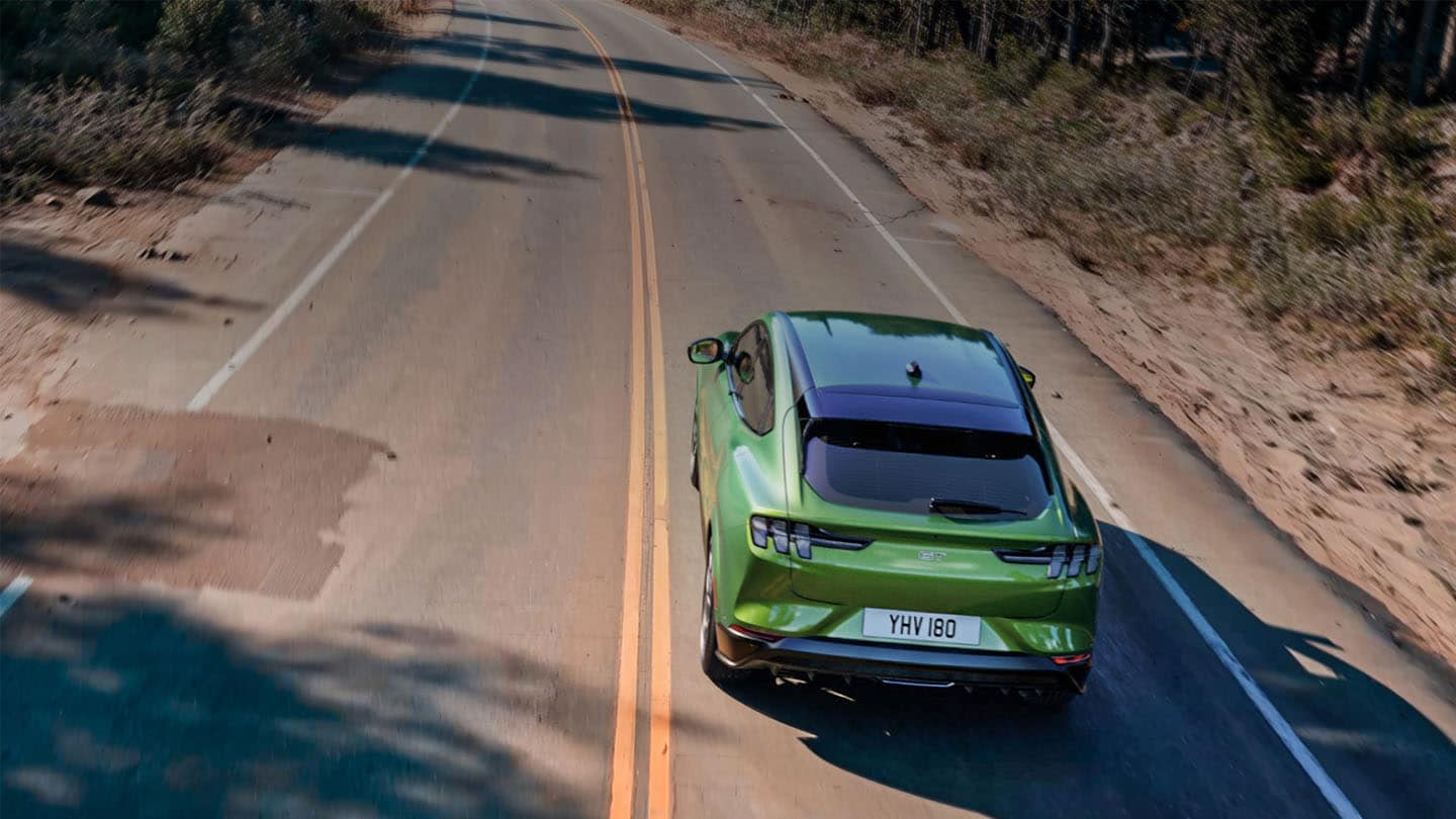 Una imagen de un Ford Mustang Mach-E GT en Eruption Green circulando por una carretera de montaña bordeada de árboles.