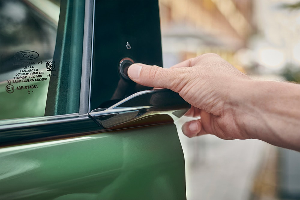 Un primer plano de una mano que opera el sistema E-Latch pulsando un botón en la puerta de un Ford Mustang Mach-E verde.