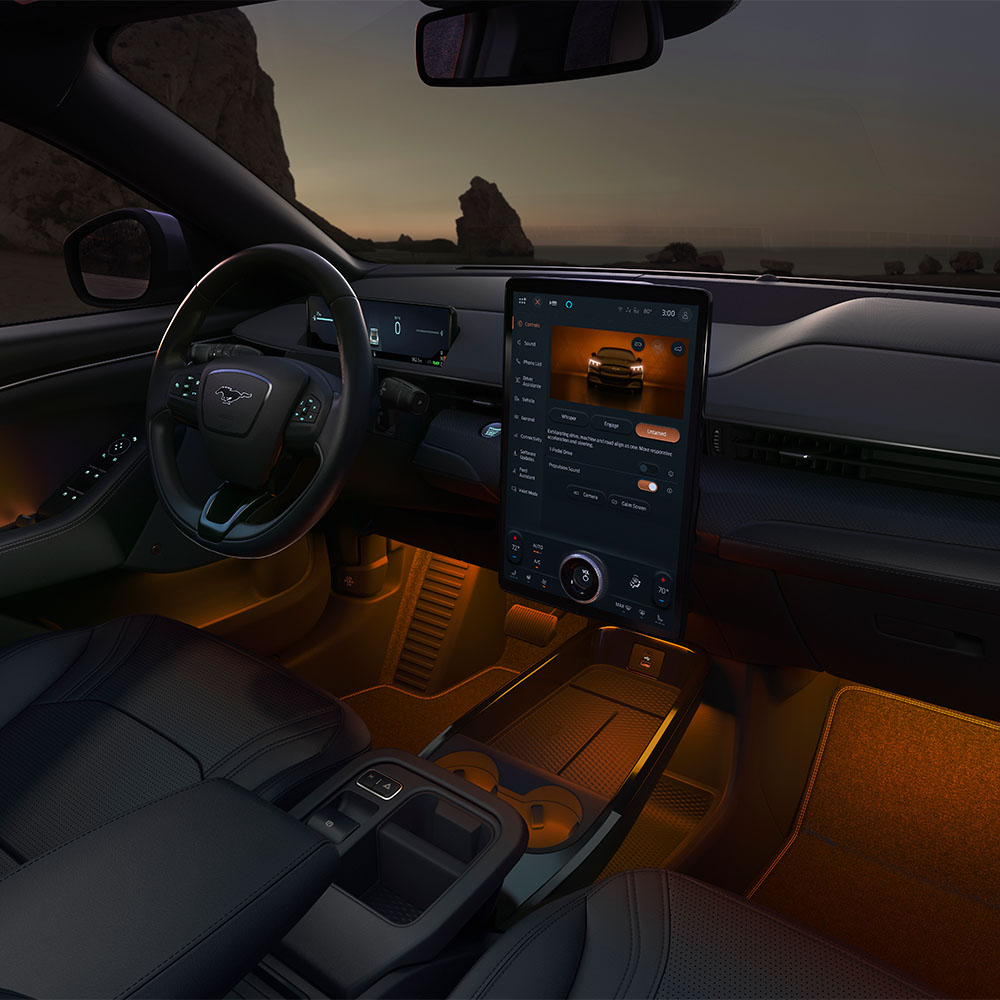 El interior del Ford Mustang Mach-E por la noche, con la pantalla táctil SYNC 4 de 15,5" y la iluminación LED ambiental en color naranja.