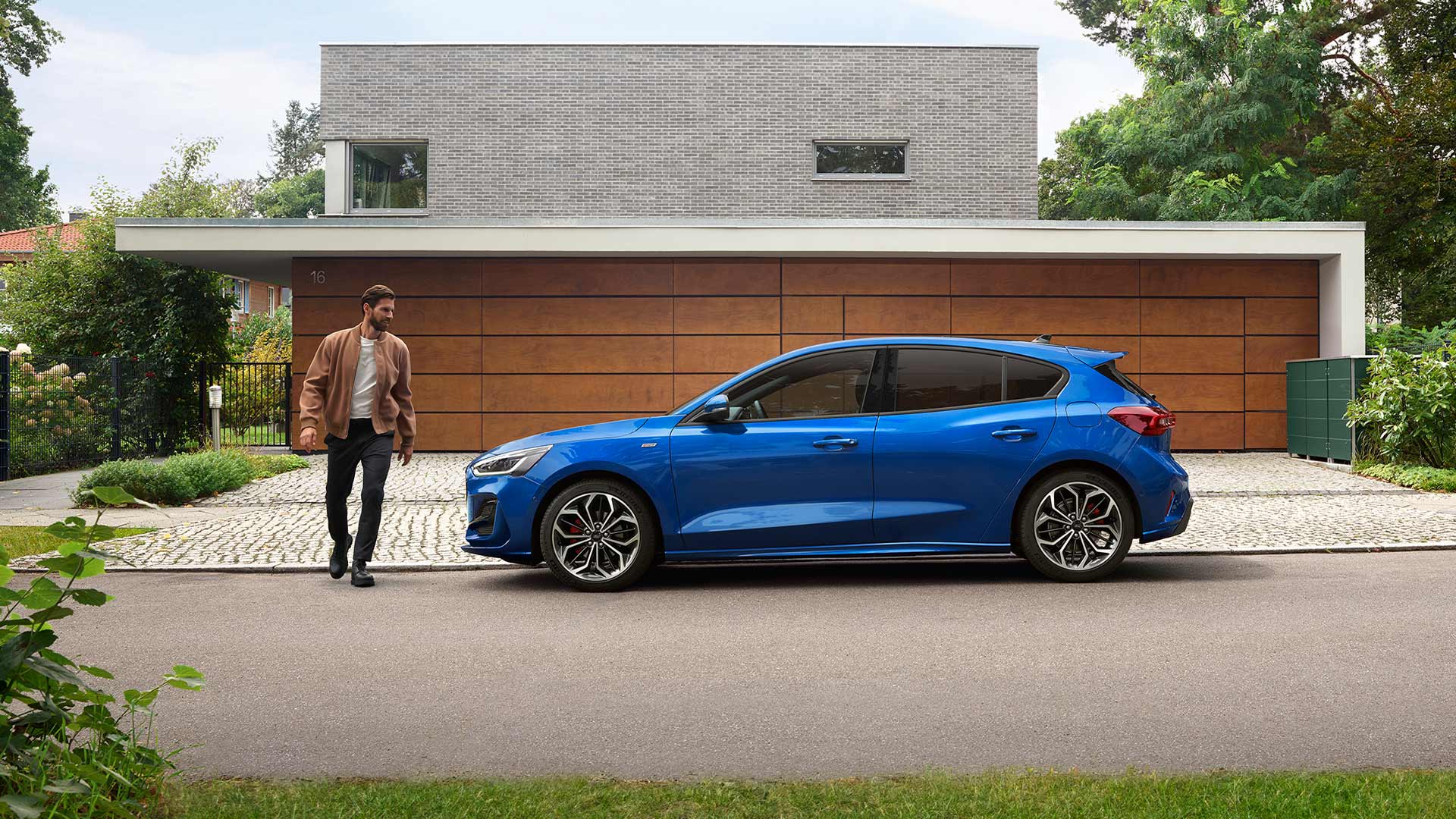 Imagen de un hombre acercándose a un Ford Focus azul aparcado en la puerta de una casa.
