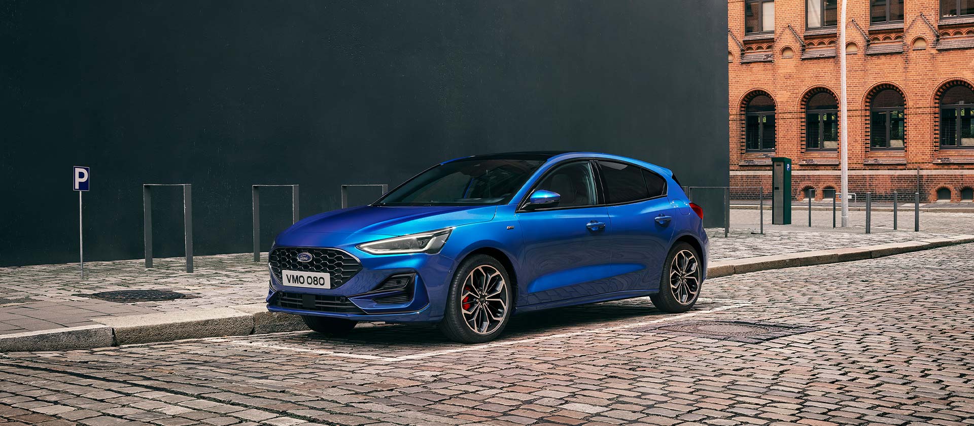 Un Ford Focus hatchback azul aparcado en una calle empedrada en un entorno urbano.