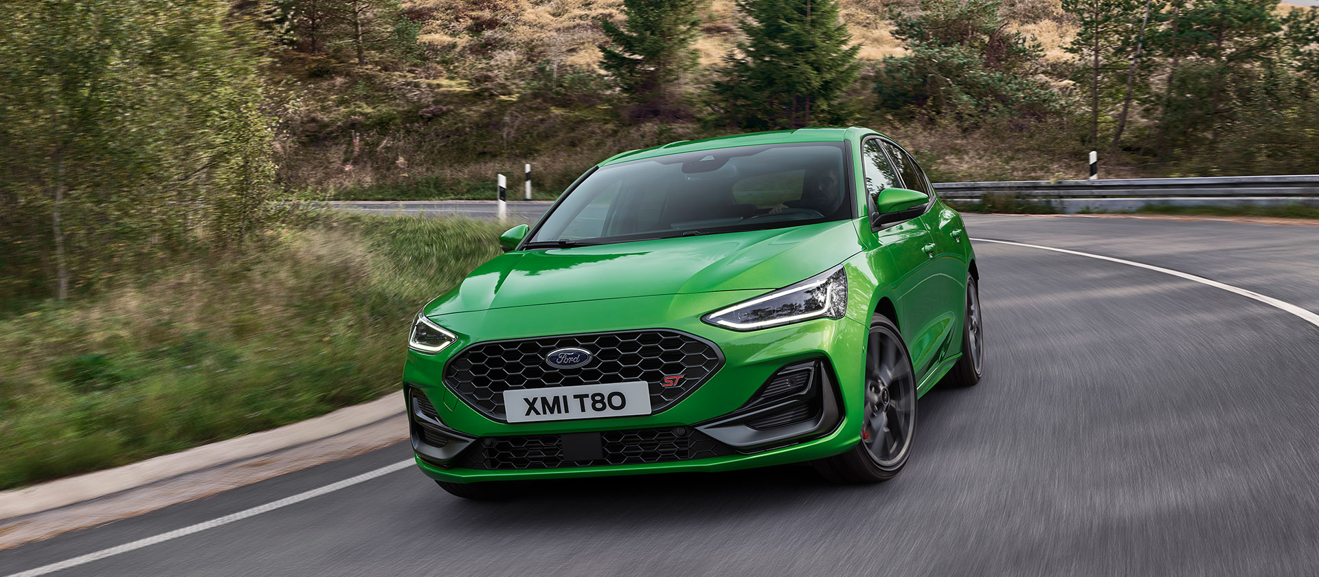 Un Ford Focus ST verde conduciendo a la vuelta de una esquina en una carretera escénica.
