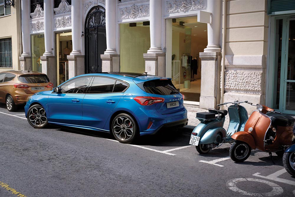 Un Ford Focus azul maniobrando hacia una plaza de aparcamiento de la ciudad utilizando la función Active Park Assist.