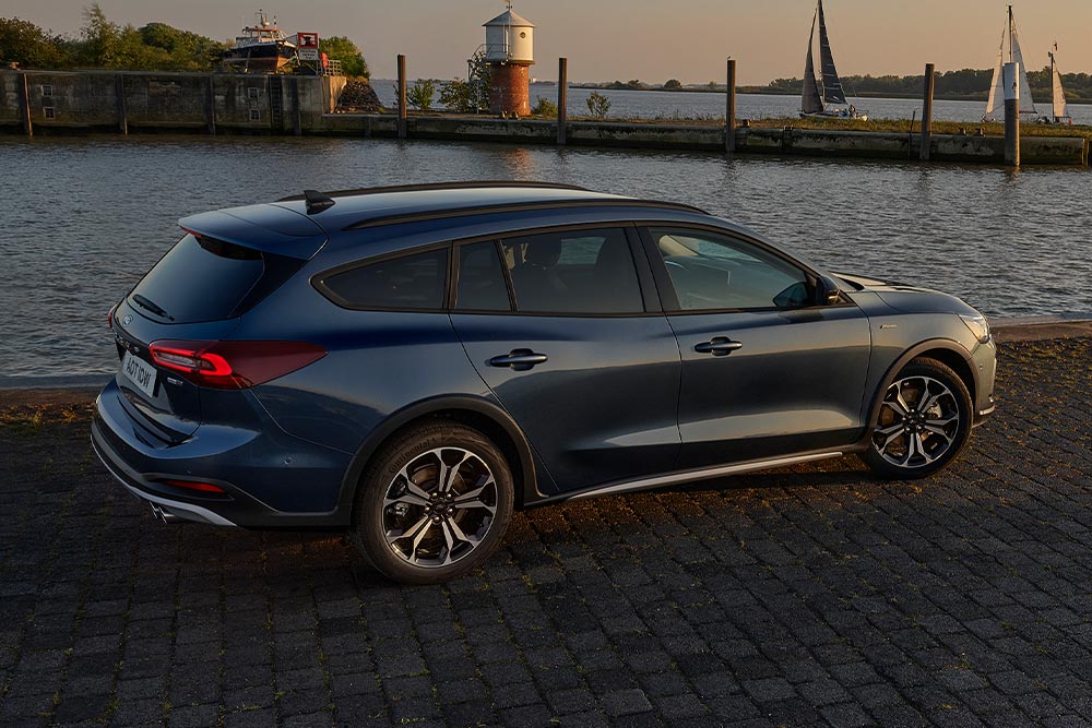 Un Ford Focus Active Estate azul oscuro aparcado junto a un cuerpo de agua al anochecer.
