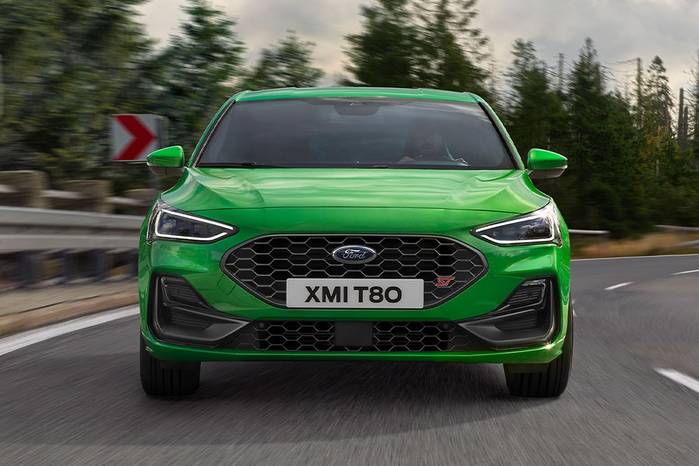 La parte delantera de un Ford Focus ST verde al doblar una esquina, con árboles borrosos en el fondo.
