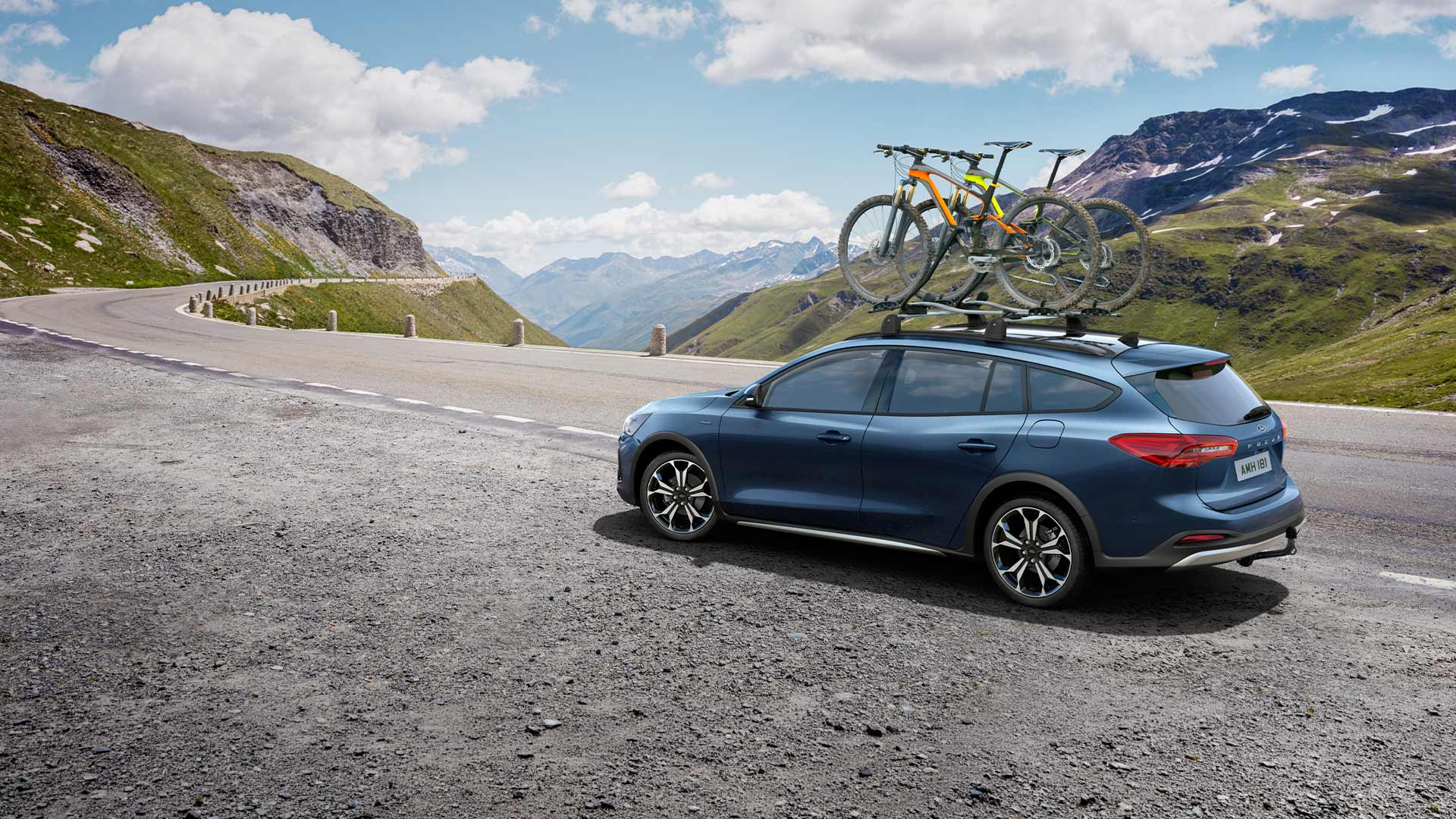 Un Ford Focus azul con bicicletas en el techo circulando por una pintoresca carretera de montaña.