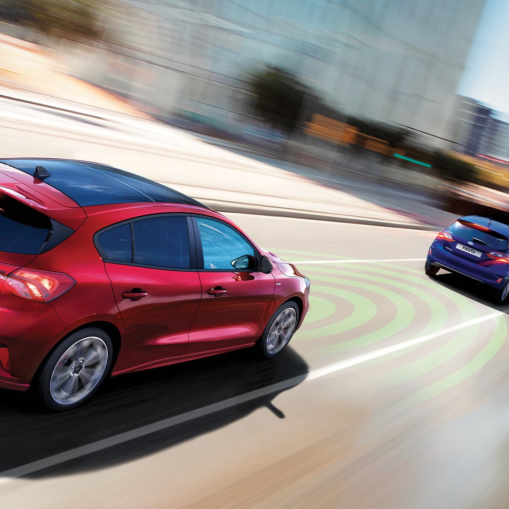 Un gráfico que muestra un Ford Focus rojo usando sensores, indicados por líneas azules, para detectar el automóvil de adelante como parte del sistema de frenado de emergencia.