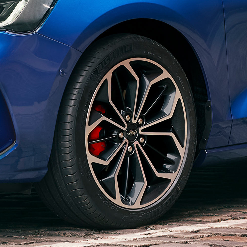 Primer plano de las llantas de aleación grises con pinzas de freno rojas en un Ford Focus azul.