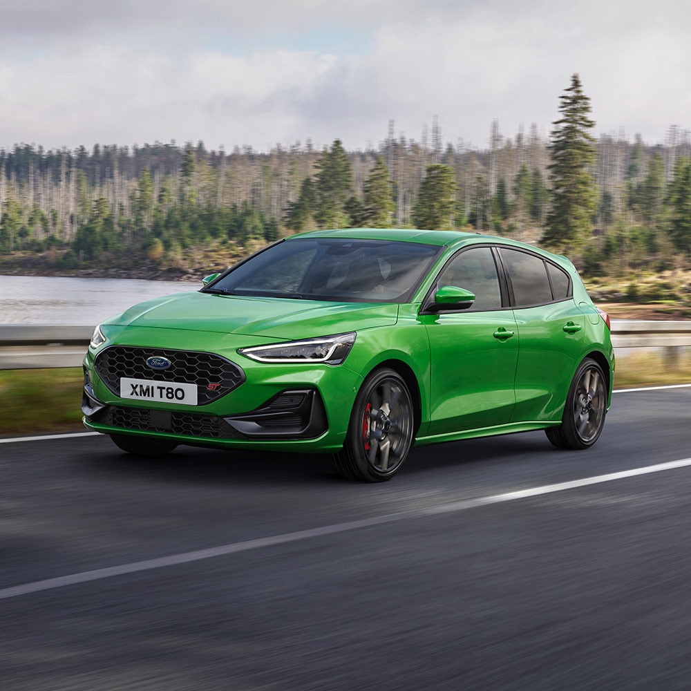 Un Ford Focus ST verde conduciendo por una carretera sinuosa rodeada de árboles.