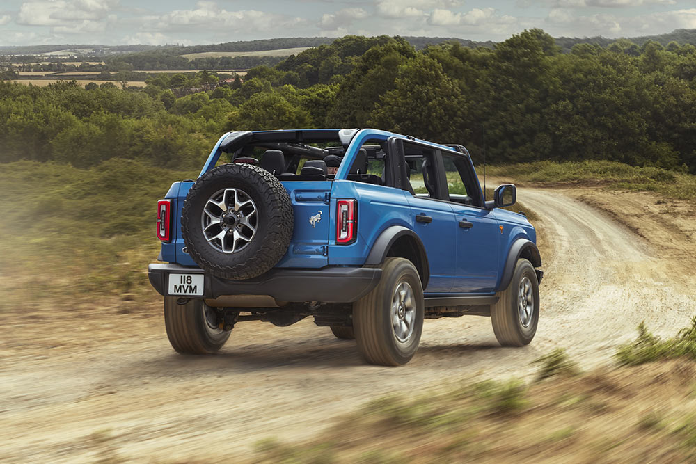 Vista trasera de un Ford Bronco azul que recorre un paisaje rural.