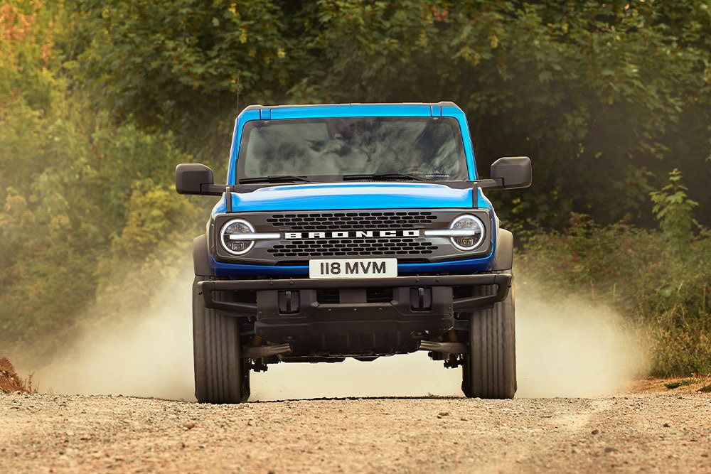 Vista delantera de un Ford Bronco azul que recorre un camino de tierra. 