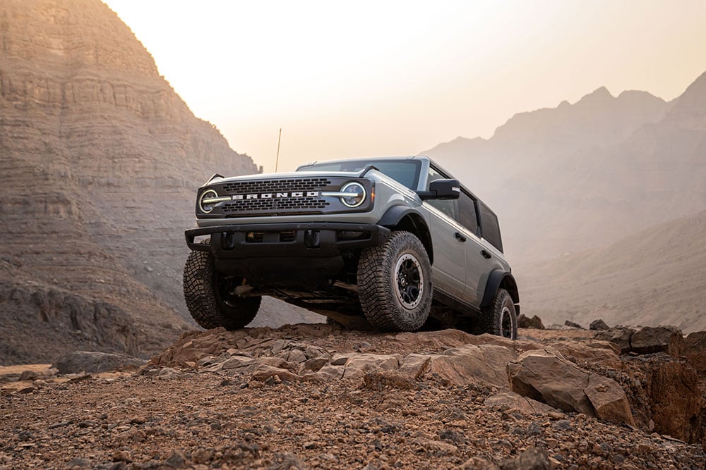 Un Ford Bronco gris aparcado en lo alto de un camino rocoso en un paisaje montañoso.
