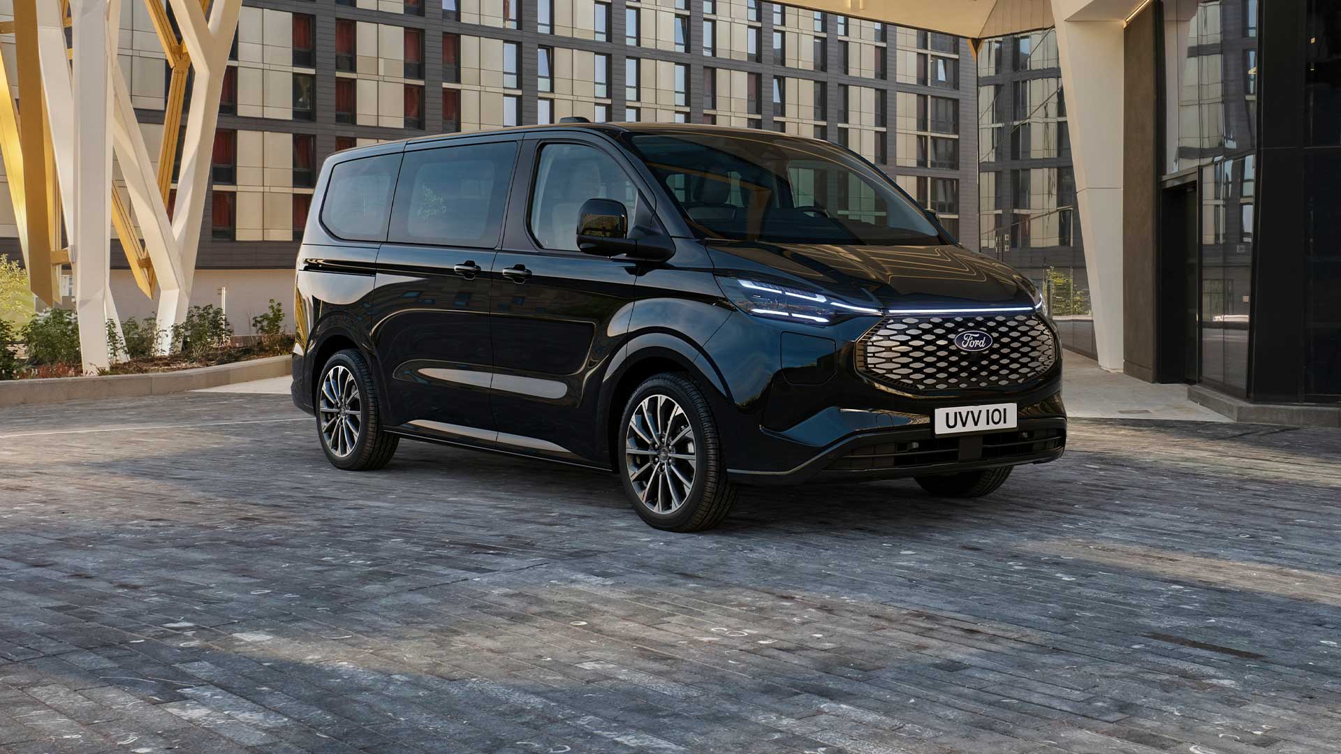 Un Ford E-Tourneo Custom negro estacionado frente a un edificio moderno.