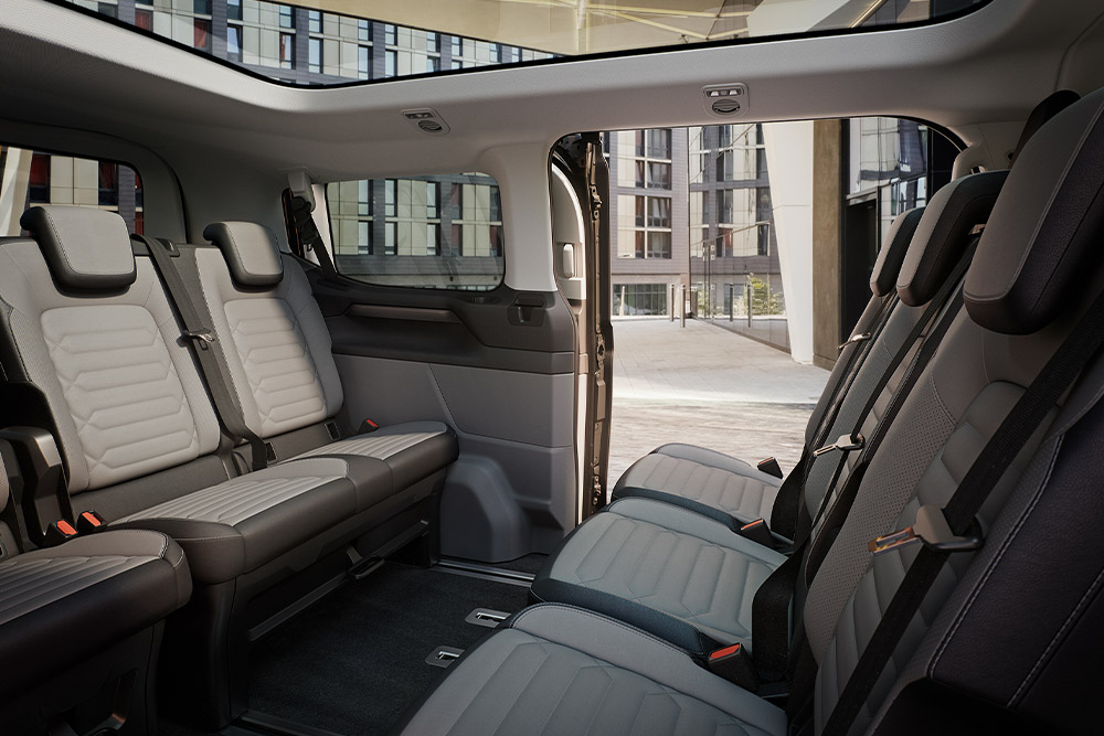 Vista interior del Ford Tourneo Custom que muestra varias filas de asientos de pasajeros grises y el techo panorámico.