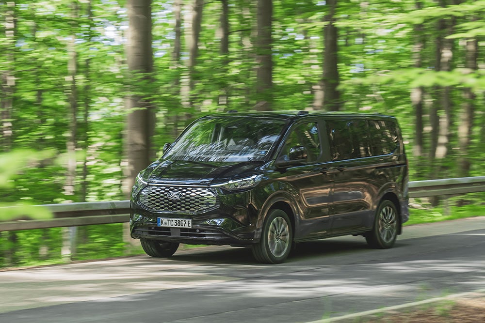 Un Ford E-Tourneo Custom negro recorriendo una carretera arbolada.