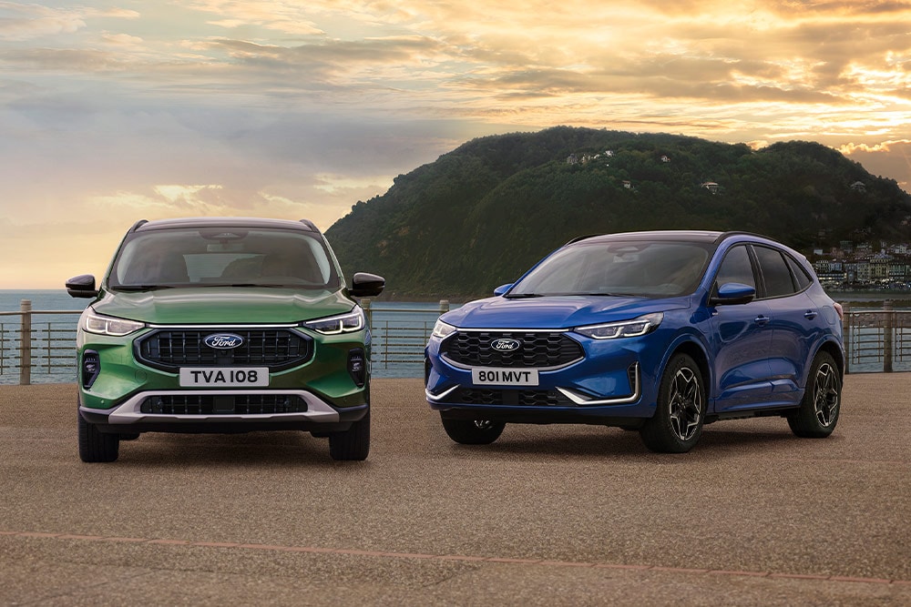Un Ford Kuga Active verde y un Ford Kuga ST Line azul aparcados, uno junto al otro, en un aparcamiento costero. 