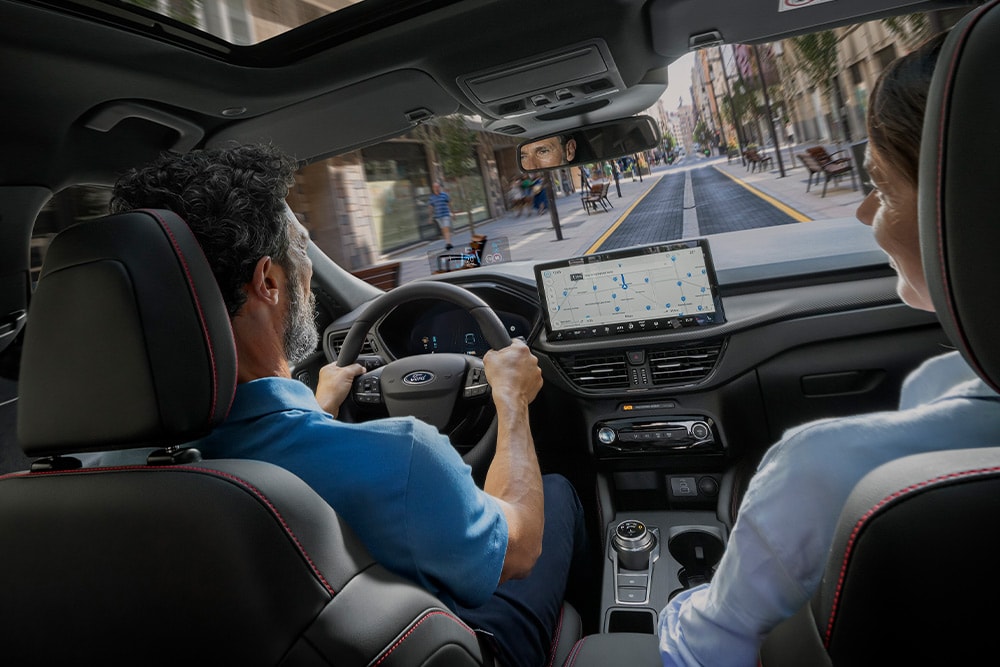 Dos personas en un Ford Kuga por una calle de la ciudad  que siguen las indicaciones de la pantalla digital de 12,3".