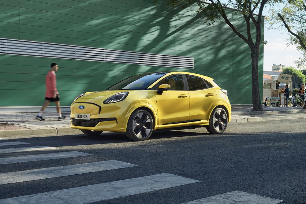 Vue latérale d’une Ford Puma Gen-E® électrique jaune stationnée au bord de la route.