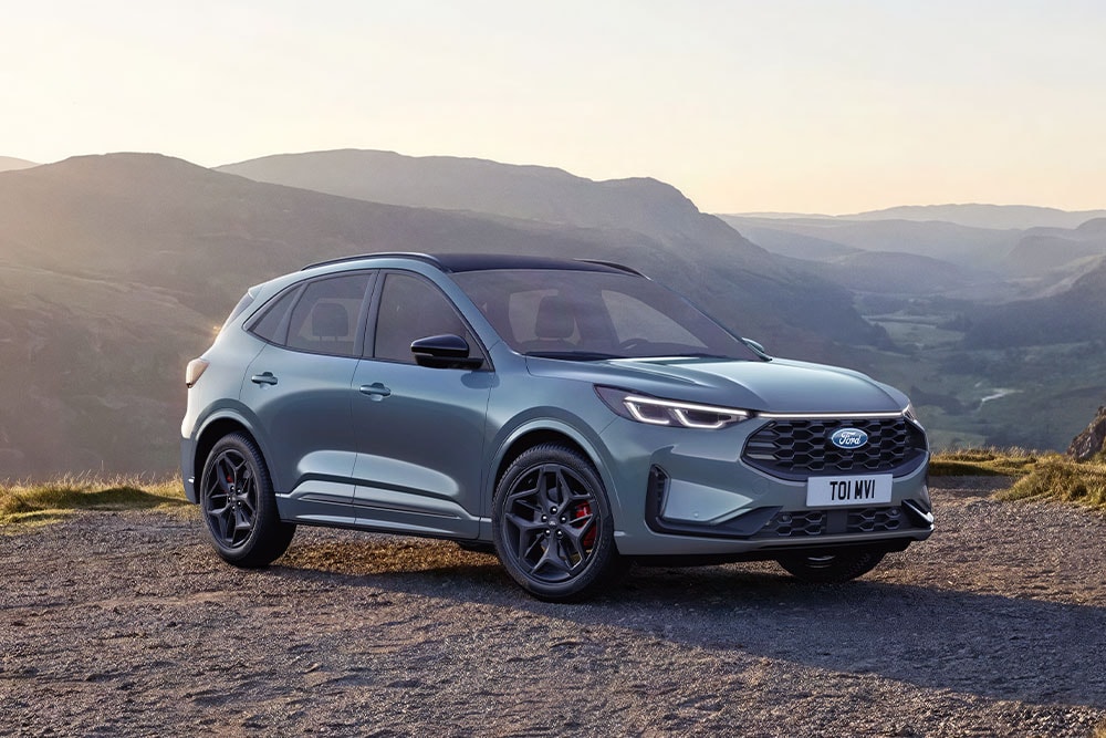 Un Ford Kuga gris aparcado en una carretera de grava de montaña al atardecer.