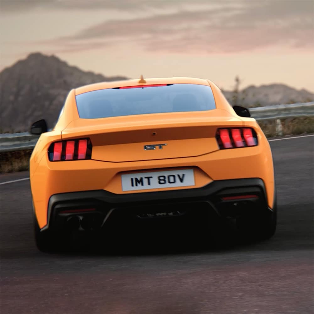 La parte trasera de un Ford Mustang GT Fastback en color Orange Fury tomando una curva cerrada en una carretera rural