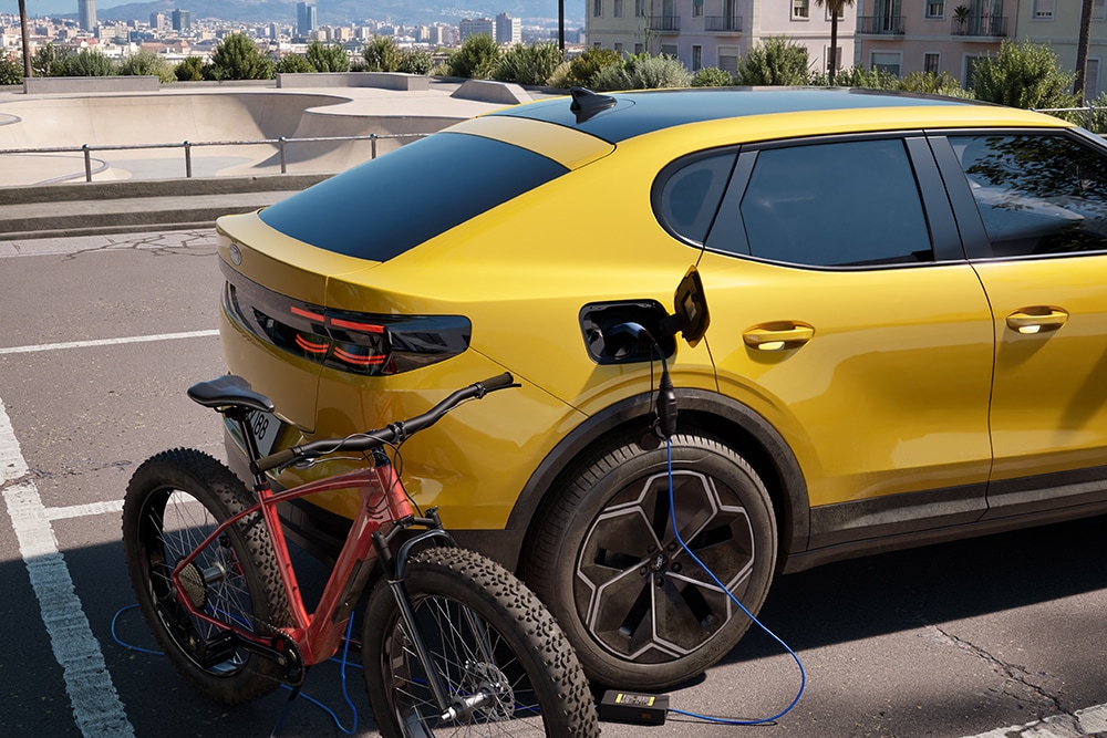 Un Ford Capri® amarillo aparcado, cargando una bicicleta eléctrica roja en un paisaje urbano.