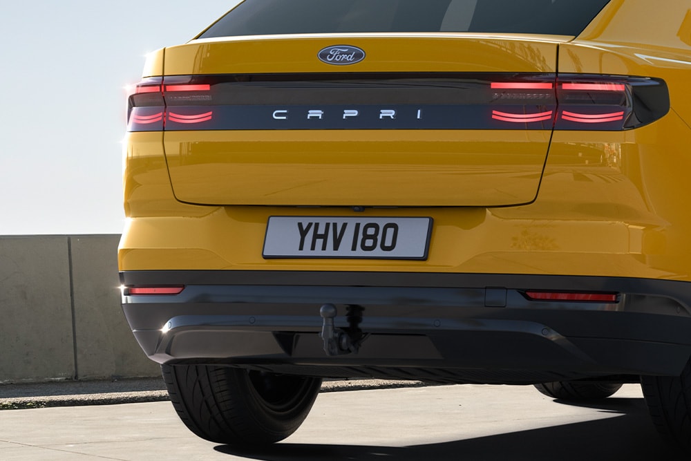 Vista de la parte trasera de un Ford Capri® amarillo circulando por una carretera en una zona urbana.