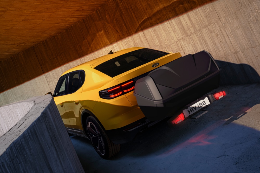 Ford Capri amarillo aparcado en una estructura de hormigón, vista trasera de una caja portaequipajes en la parte trasera con un portaequipajes.
