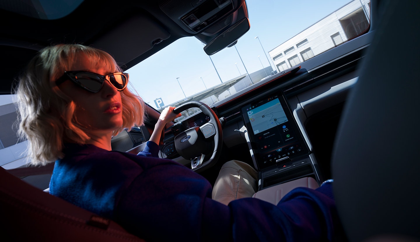 Primer plano de una mujer con las manos sobre el volante de un Ford Capri estacionado, donde puede verse asimismo el cuadro de instrumentos digital del vehículo.