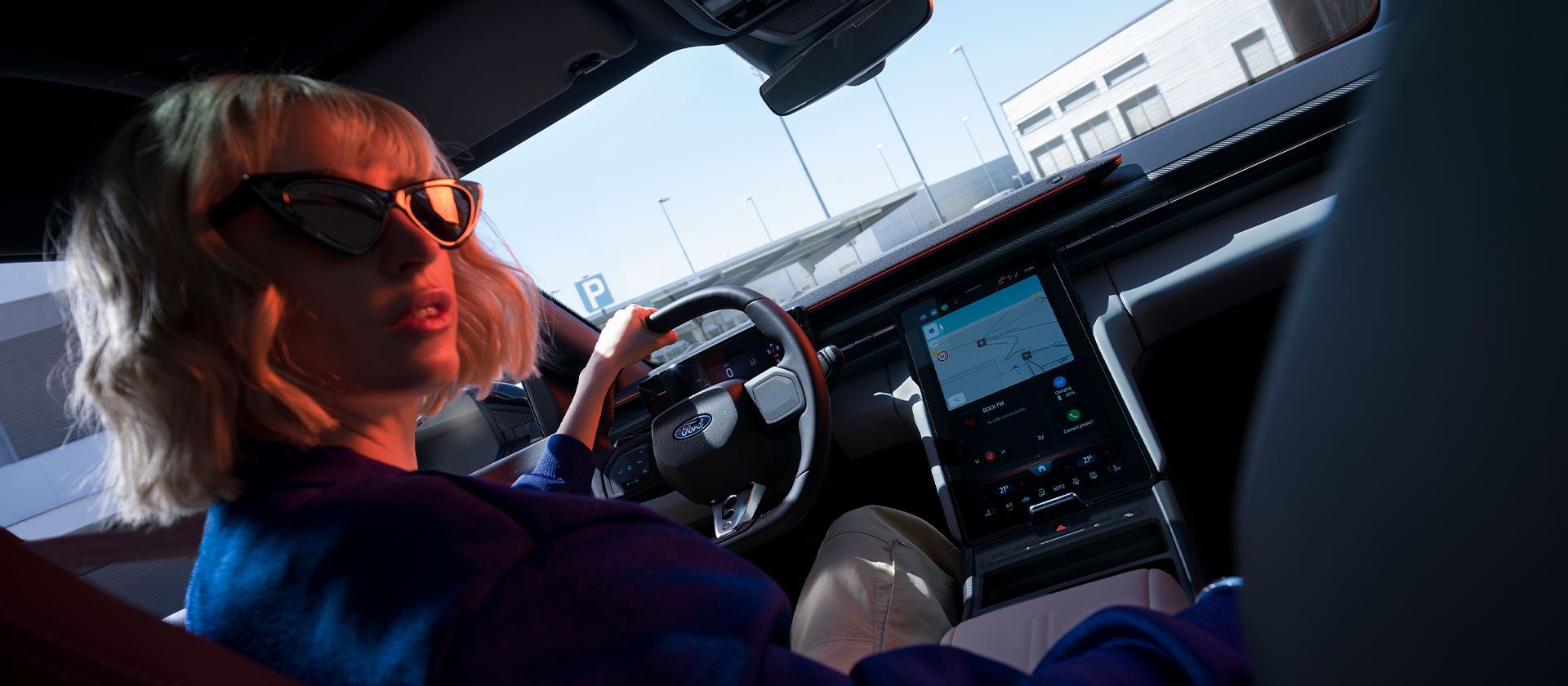 Mujer sentada en el asiento del conductor de un Ford Capri® estacionado con vistas del volante y la gran pantalla táctil SYNC® Move.