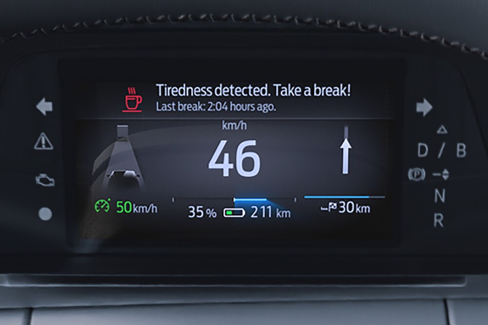 Cuadro de instrumentos digital del Ford Capri mostrando la velocidad del vehículo y un mensaje de alerta al conductor recomendando a este que se tome un descanso.