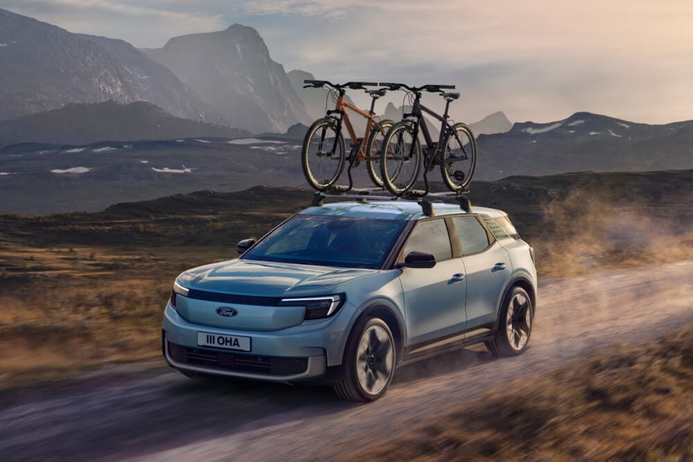 Ford Explorer azul circulando por un camino de tierra, con barras transversales, un portabicicletas de techo y dos bicicletas montadas en el techo.