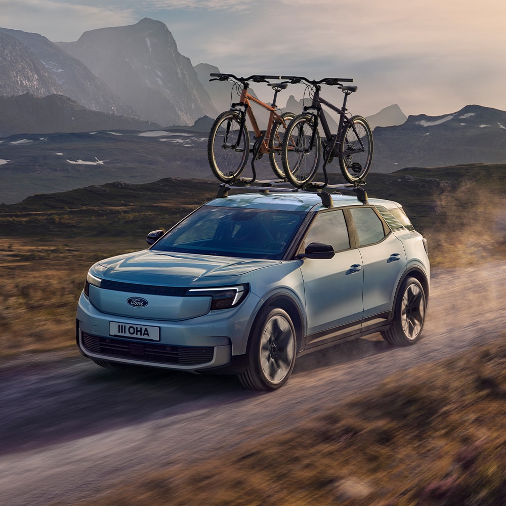Ford Explorer azul circulando por un camino de tierra, con barras transversales, un portabicicletas de techo y dos bicicletas montadas en el techo.