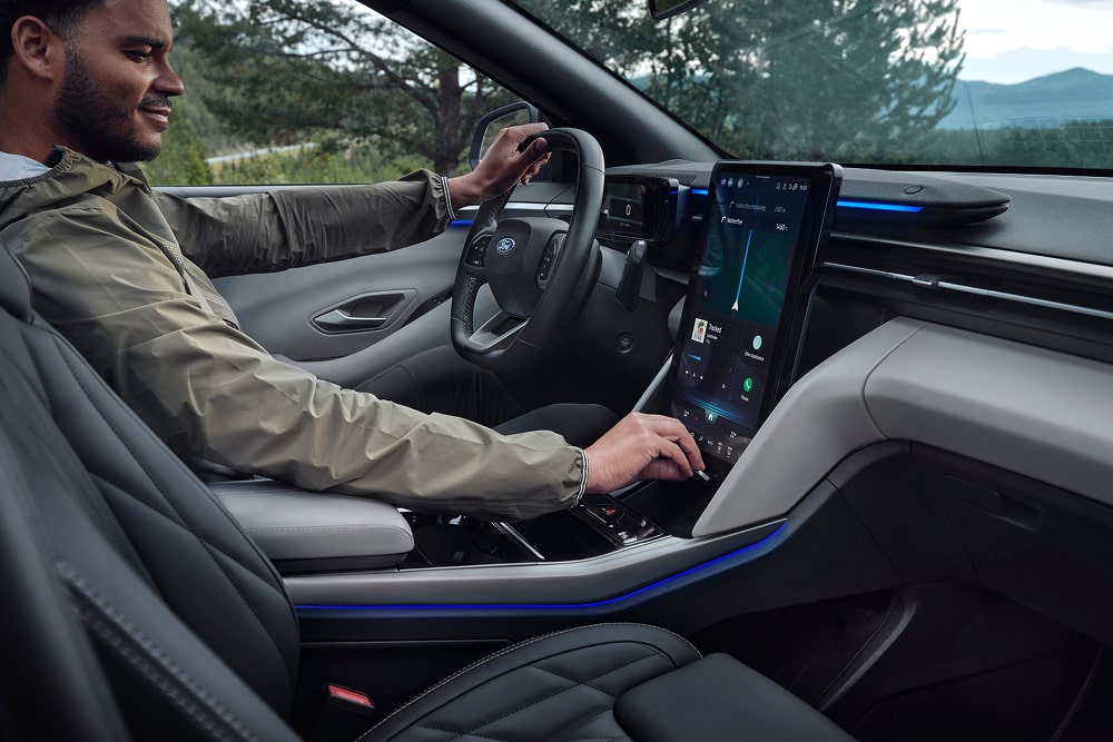 Imagen de un conductor que utiliza el sistema de infoentretenimiento con pantalla táctil dentro del SUV familiar Ford Explorer.