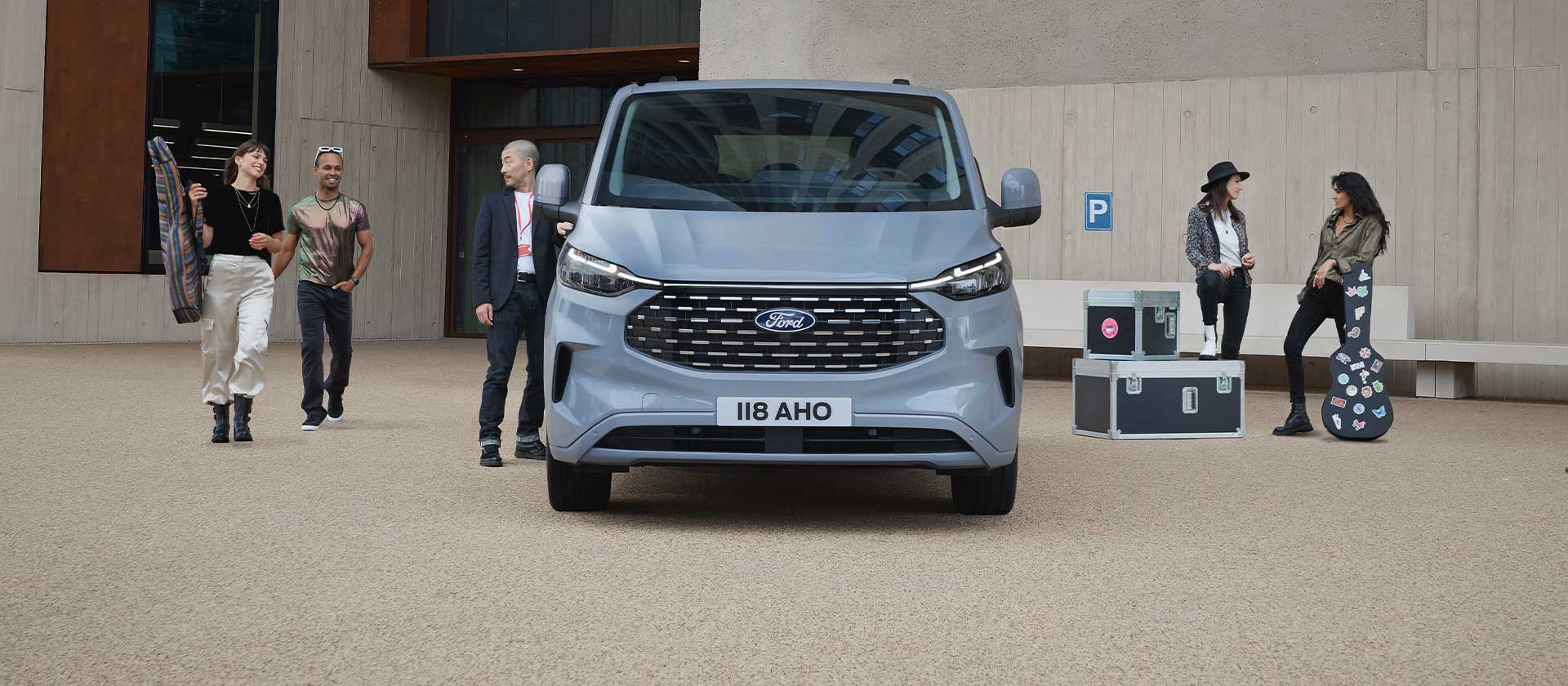 Un grupo de personas de pie con instrumentos musicales y equipos, cerca de un Ford Tourneo Custom plateado.