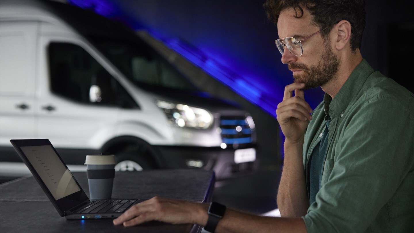 Persona trabajando en el portátil con la Ford E-Transit al fondo